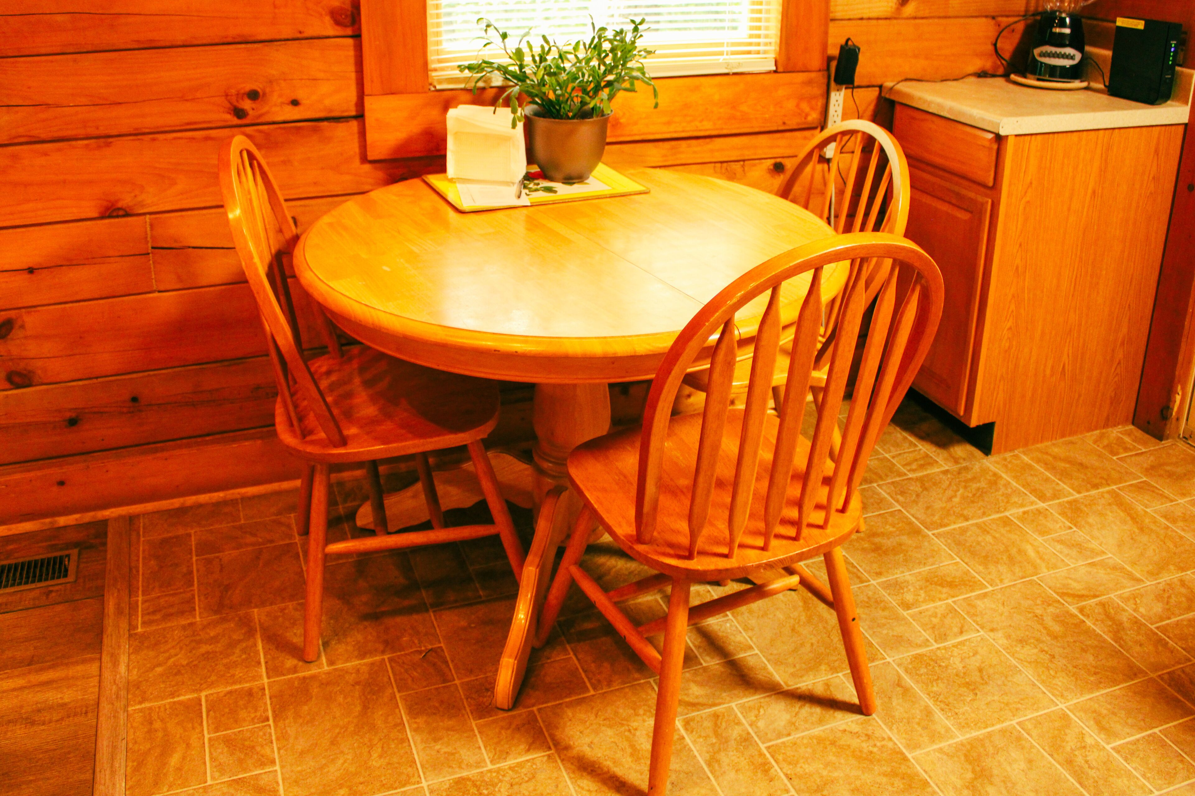 Una mesa de madera para comer con cuatro sillas, una planta en maceta y una cafetera en la encimera.