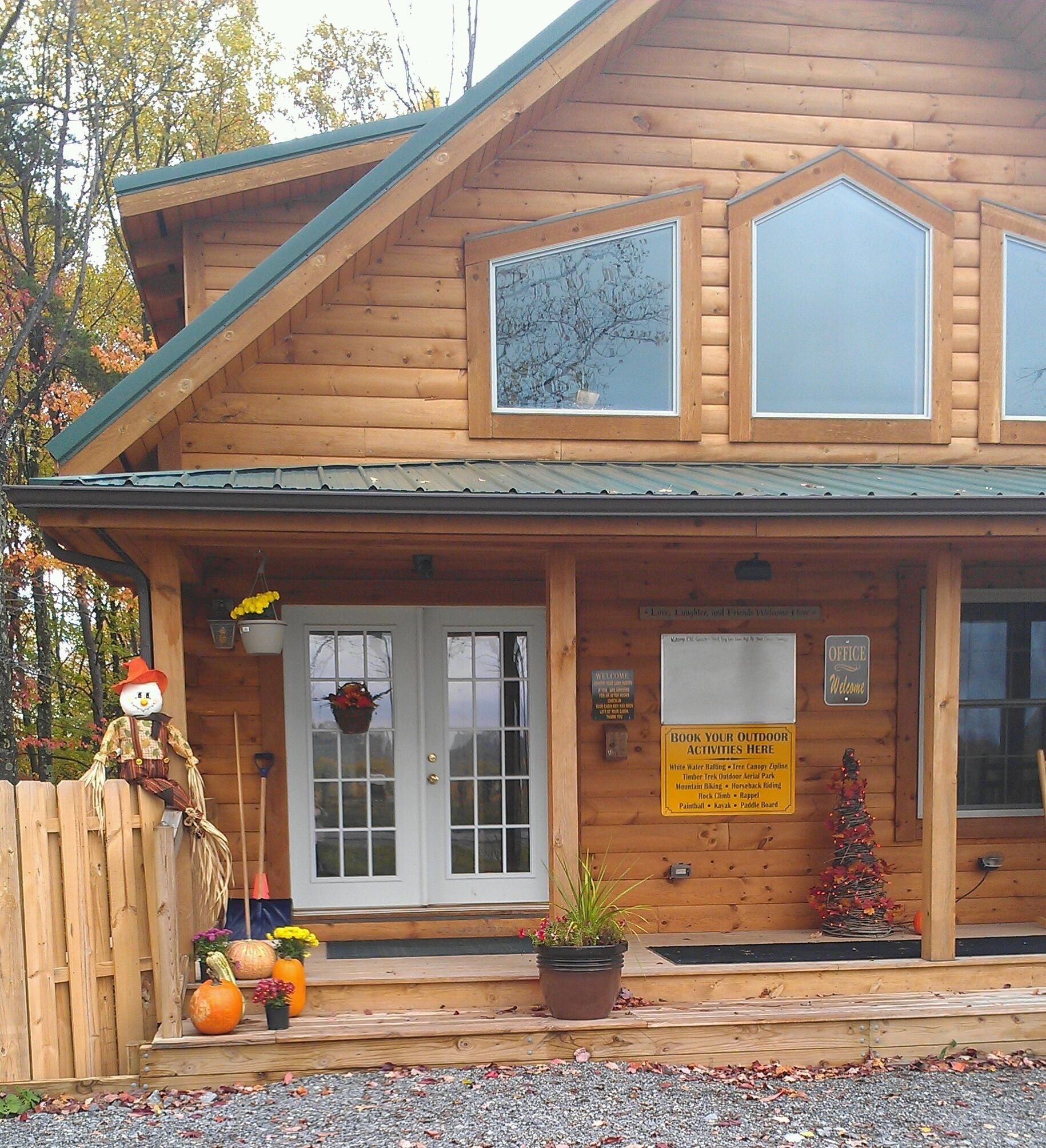 A wooden cabin with a porch, a welcome sign, and a sign listing outdoor activities.