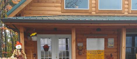 A wooden cabin with a porch, a welcome sign, and a sign listing outdoor activities.