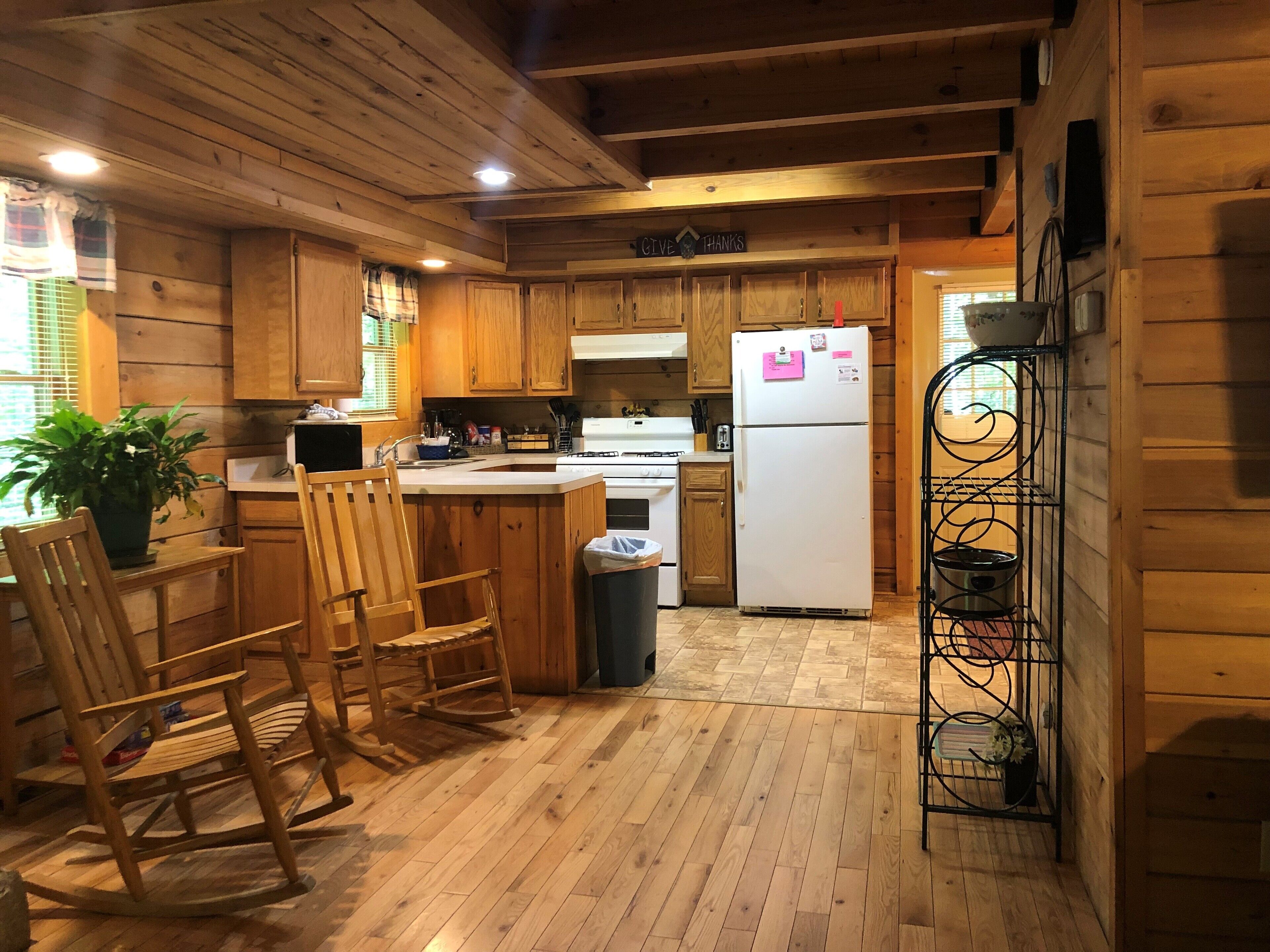 A wooden cabin kitchen with wooden cabinets, a refrigerator, a sink, and a dining area with chairs.