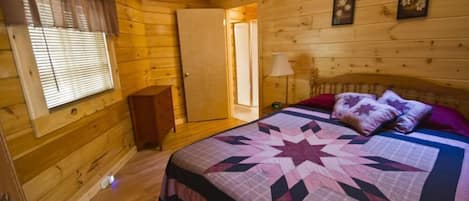 A wooden cabin bedroom with a bed, a nightstand, a lamp, and a window with blinds.