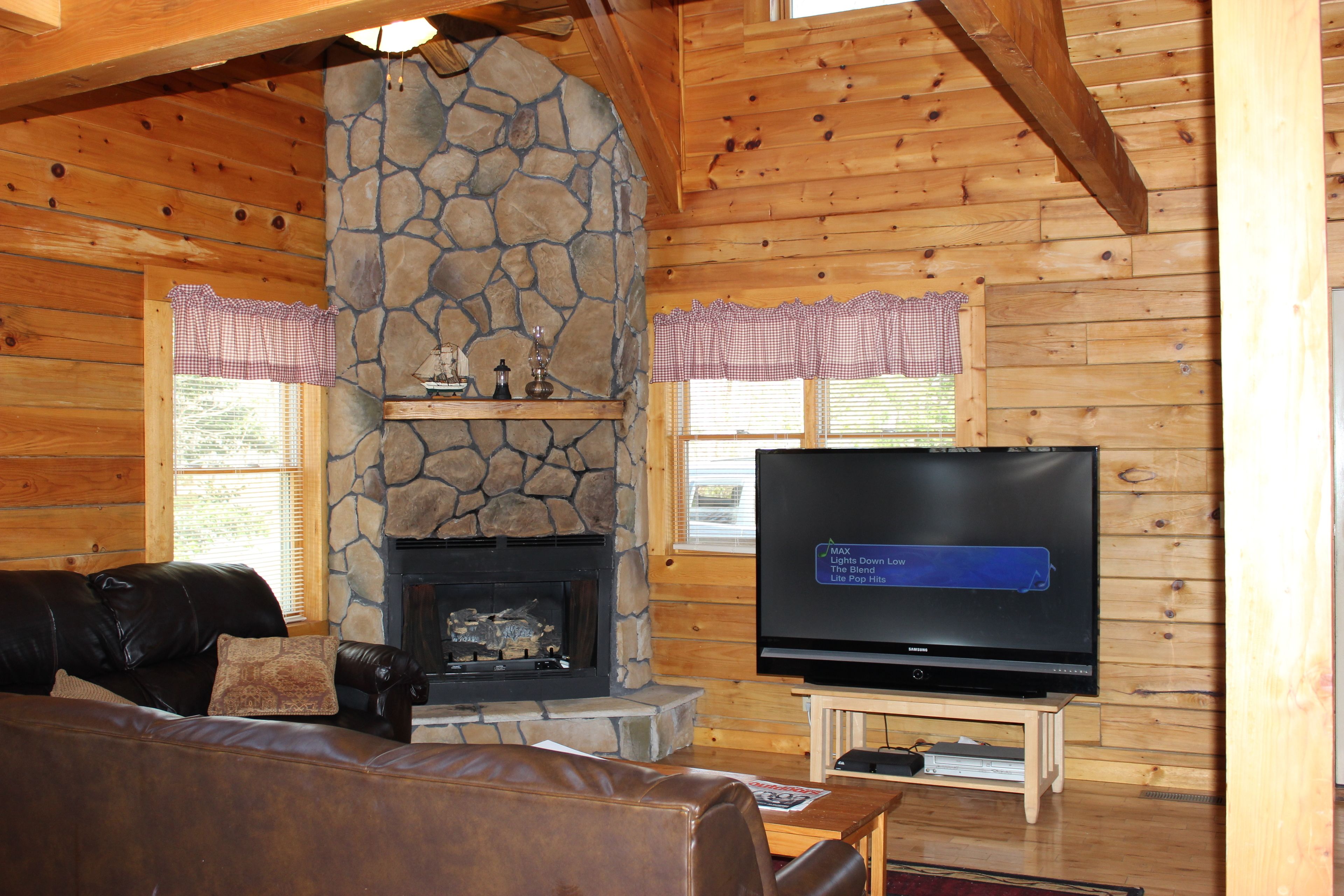 A cozy living room with a stone fireplace, a leather sofa, and a flat-screen TV on a wooden stand.