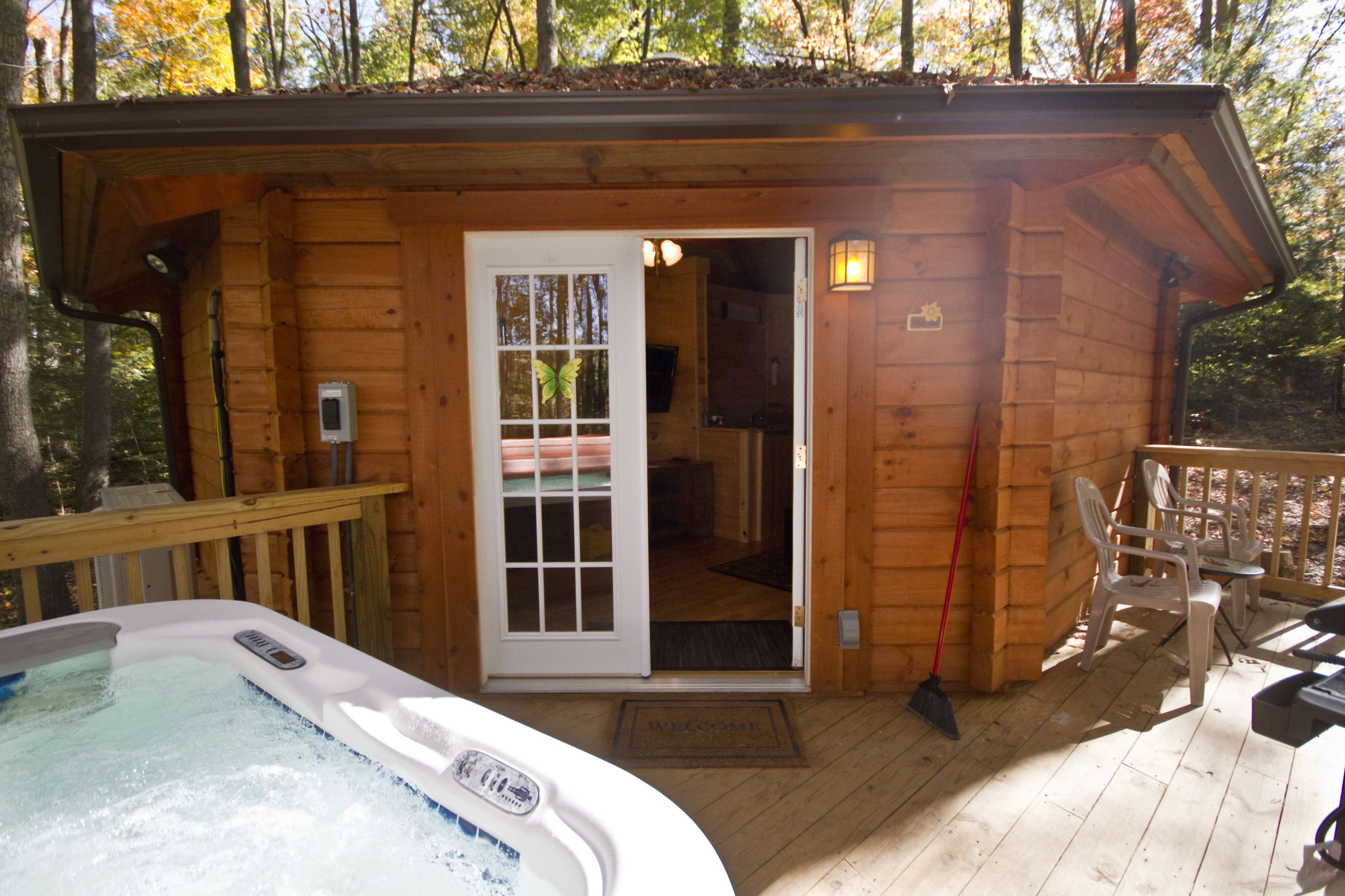 A wooden cabin with a hot tub, a deck, and a door leading to an interior room.