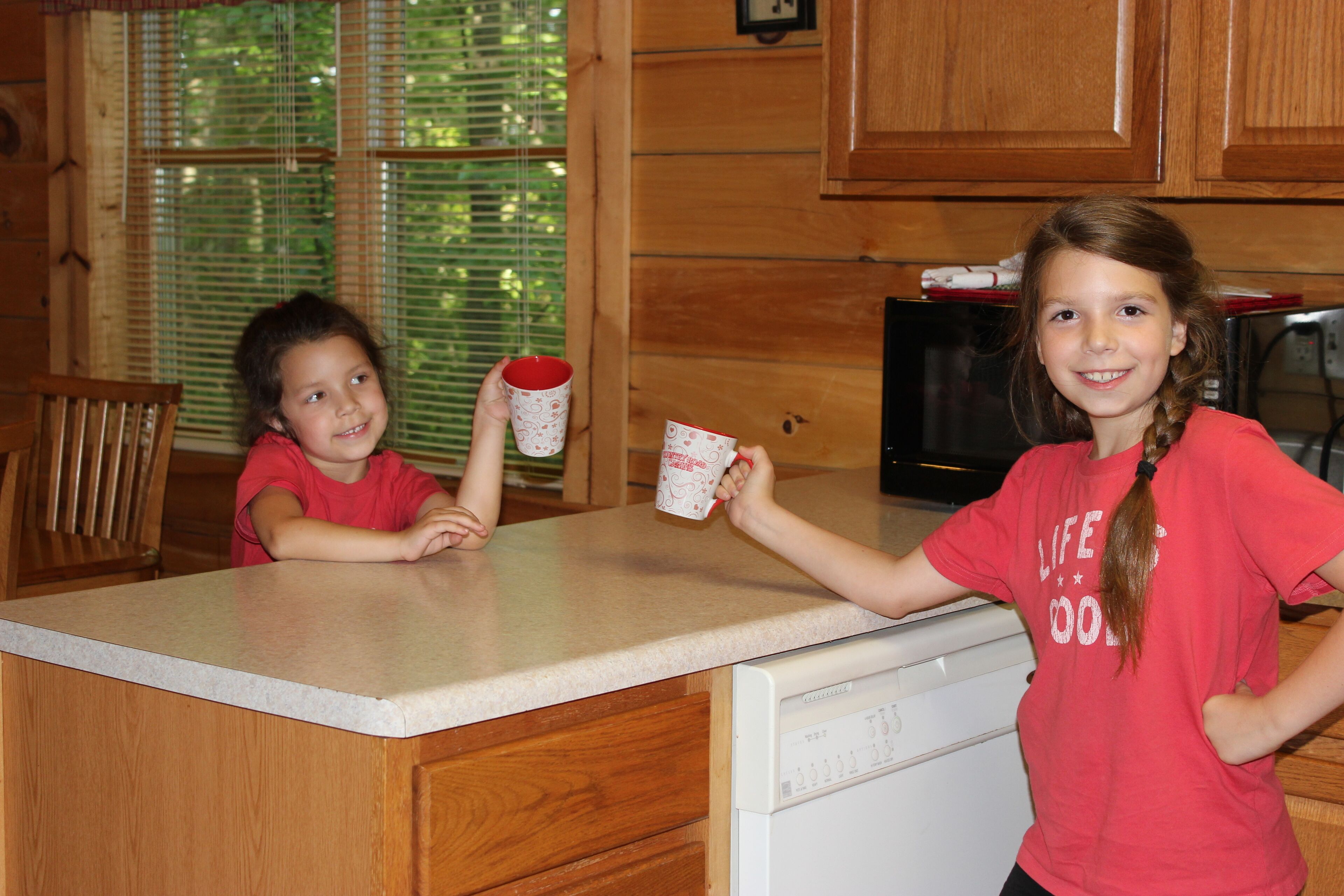 Two children in a kitchen with wooden cabinets and a dishwasher.