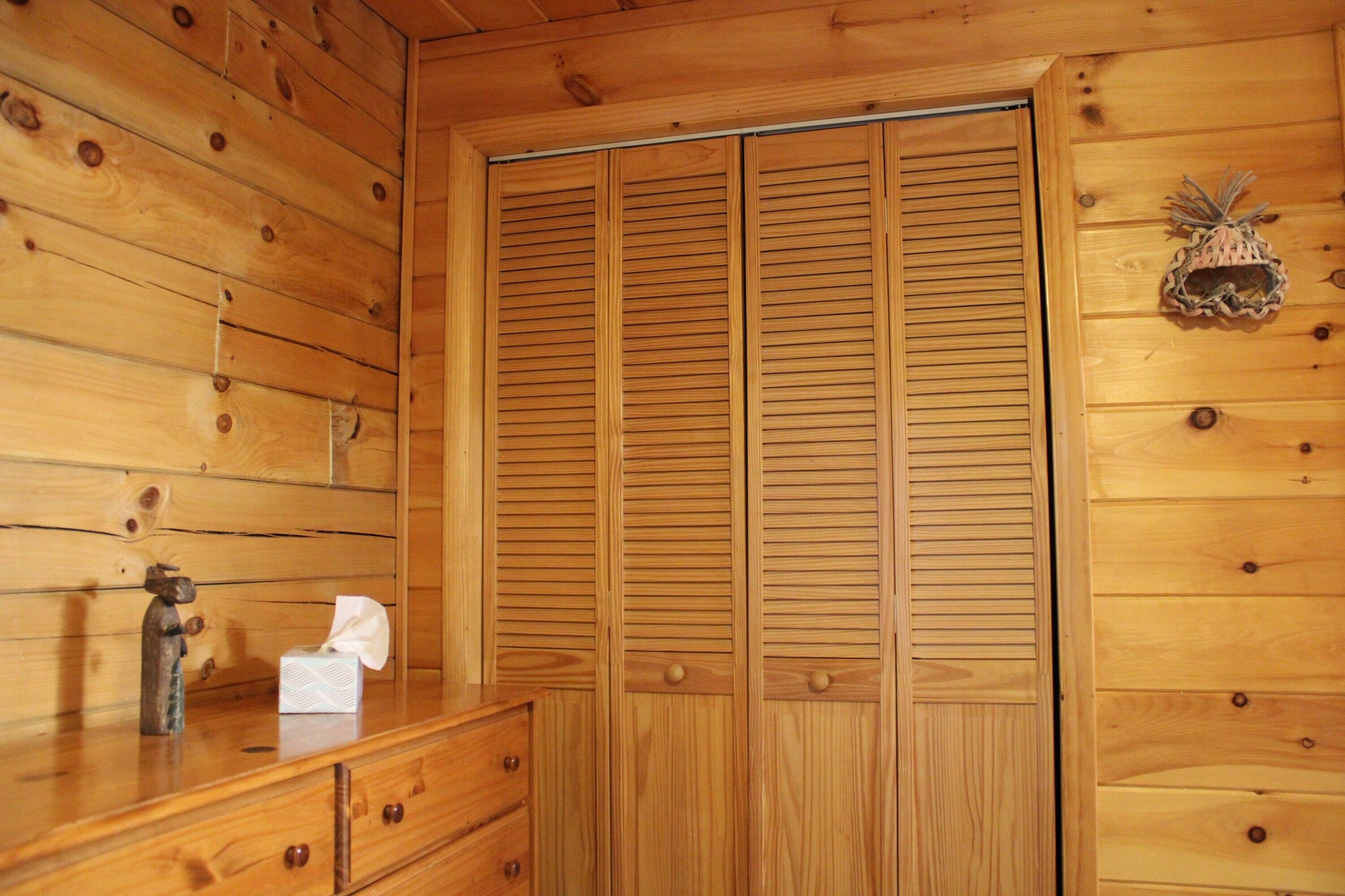 Una habitación de madera con un aparador de madera, un espejo y un armario de madera con puertas persianas.
