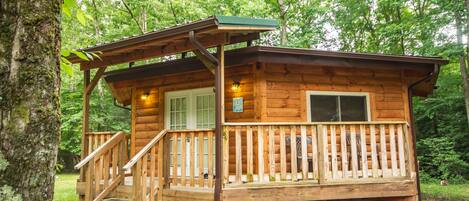 A wooden cabin with a porch, a staircase, and a window.