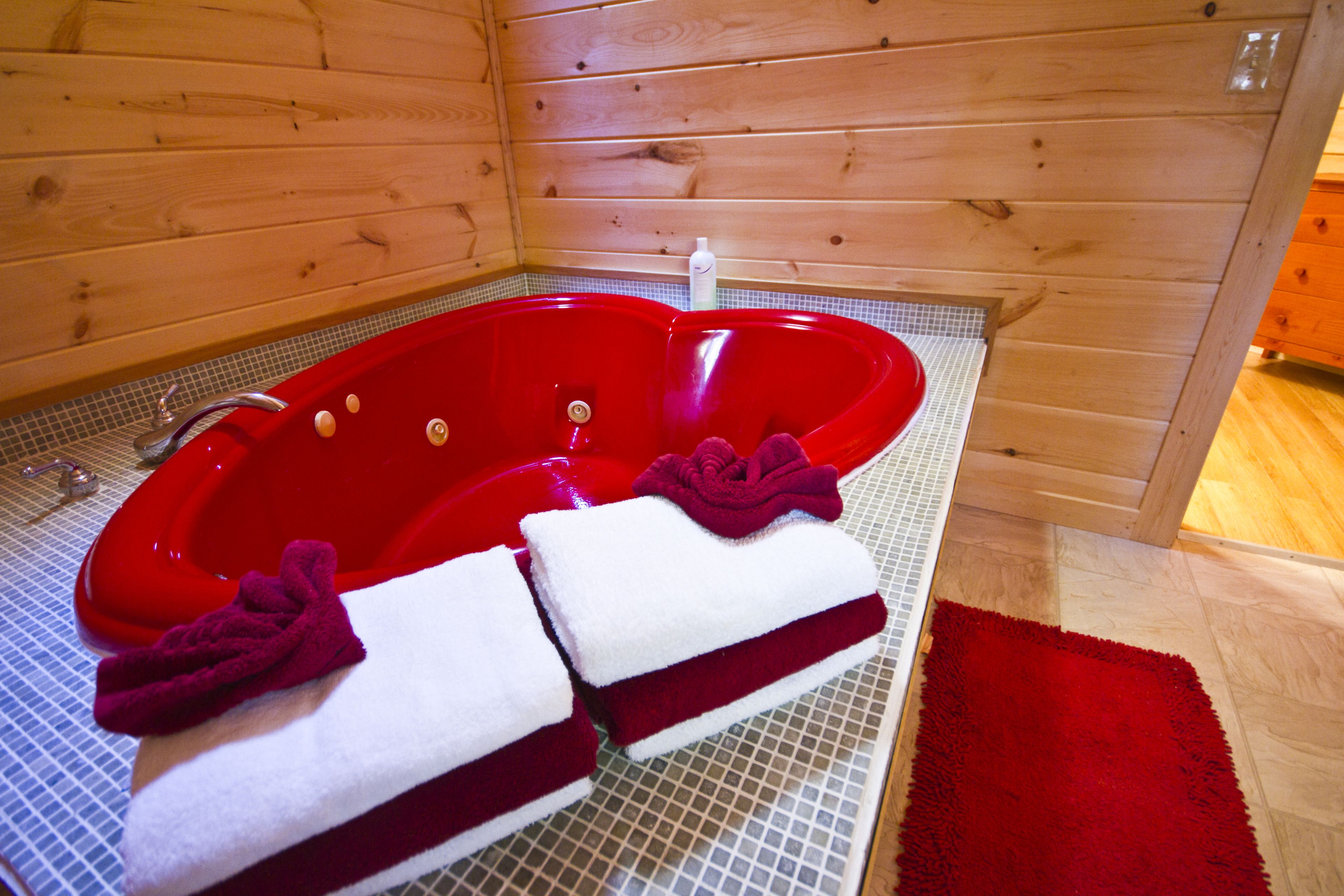Un jacuzzi rouge dans un chalet en bois, avec deux serviettes et un tapis rouge.