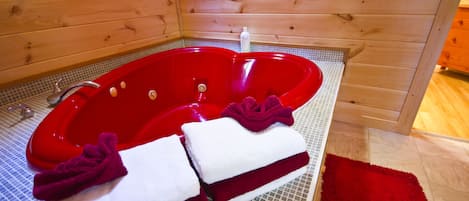 Un jacuzzi rouge dans un chalet en bois, avec deux serviettes et un tapis rouge.