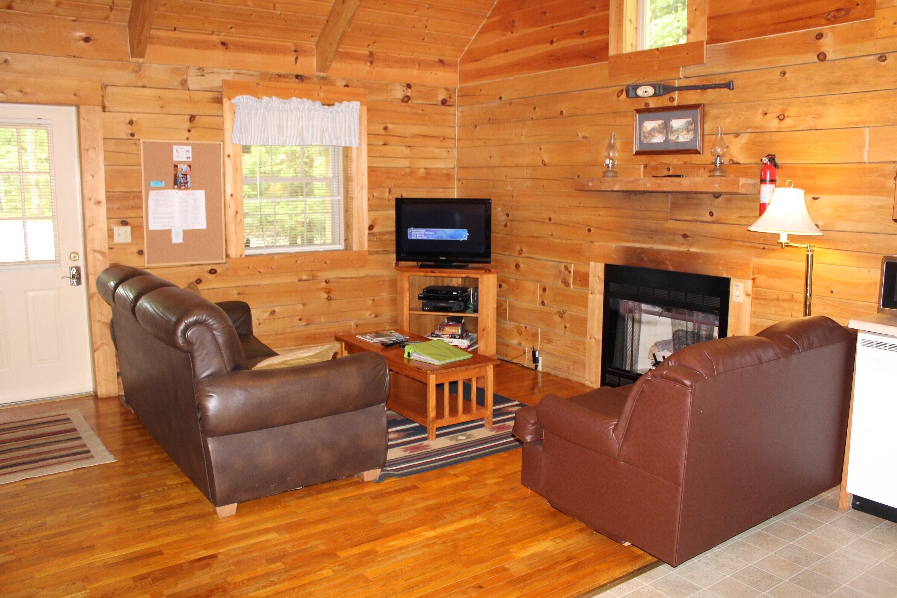 Interior acogedor de una cabaña con detalles de madera, una chimenea, un televisor y dos sofás de cuero.