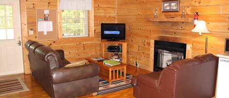 Interior acogedor de una cabaña con detalles de madera, una chimenea, un televisor y dos sofás de cuero.