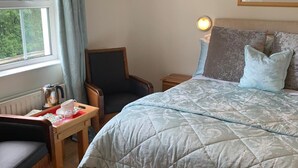 A bedroom with a large bed, a chair, a bedside table with a lamp, and a window with curtains. - Brooke Lodge Guesthouse (Magherafelt)