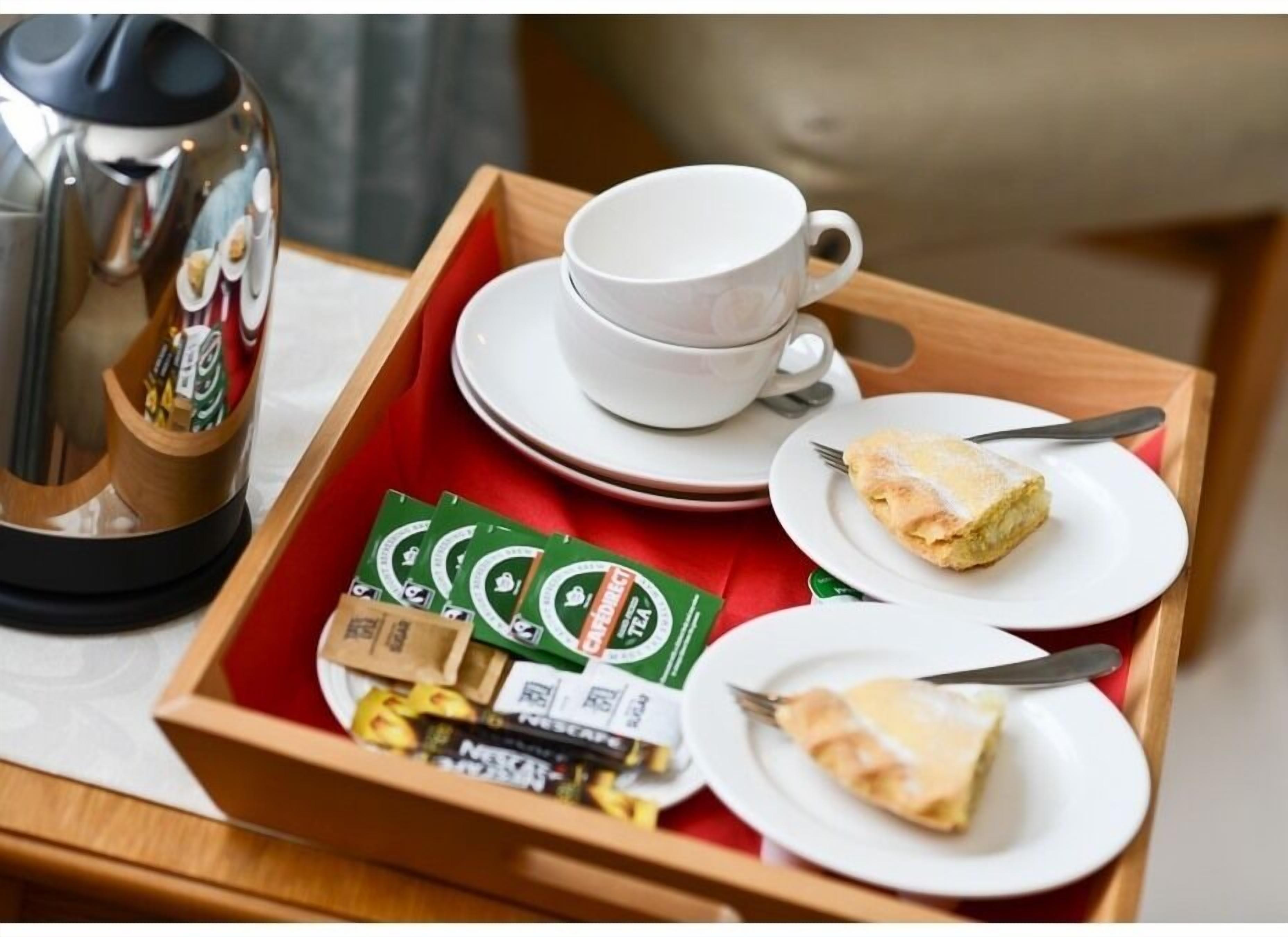 A tray with a coffee maker, cups, saucers, and food items.