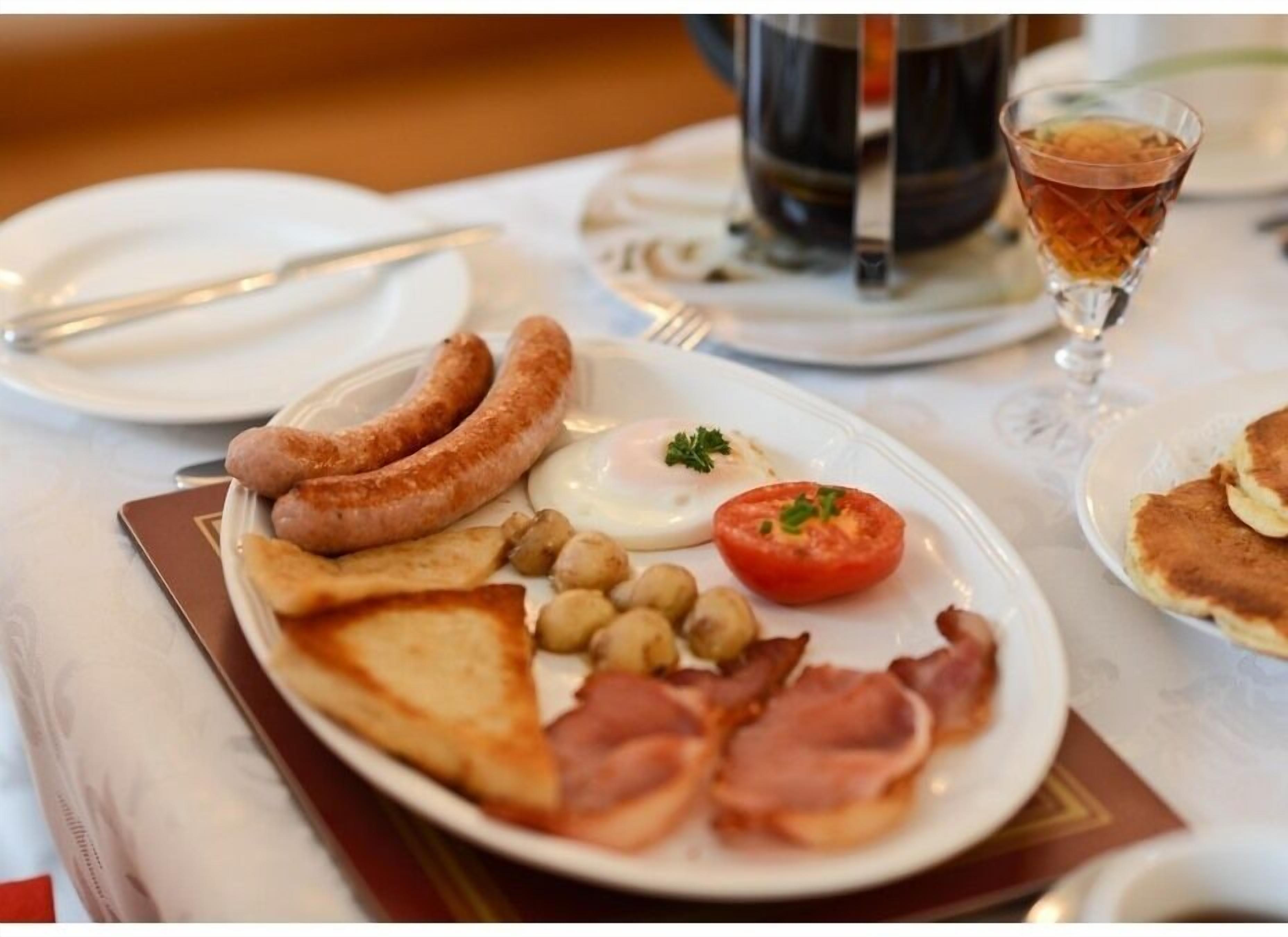 Une assiette de petit-déjeuner comprenant des saucisses, des œufs, des tomates et du bacon.
