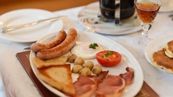 Une assiette de petit-déjeuner comprenant des saucisses, des œufs, des tomates et du bacon.