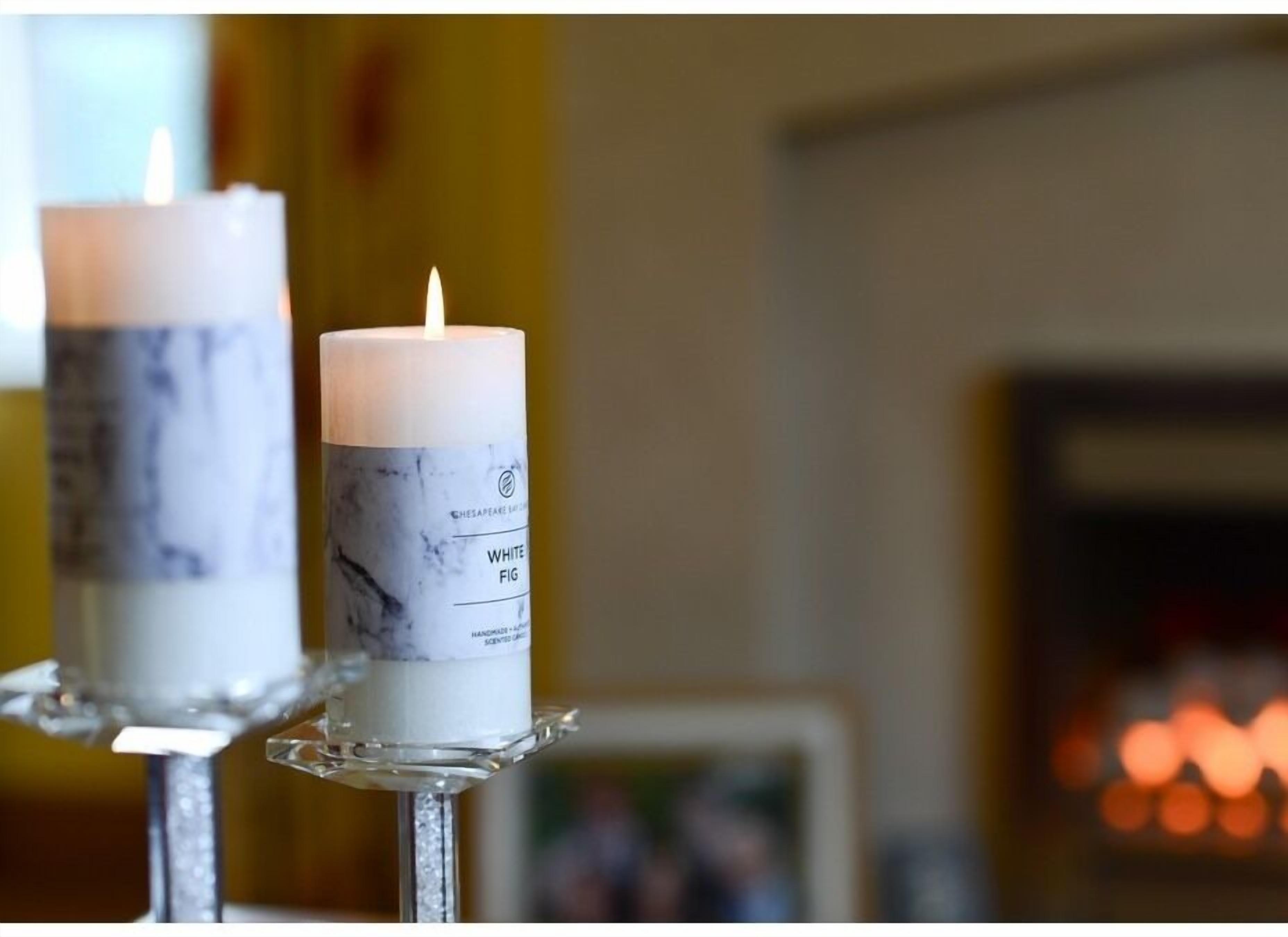 Dos velas blancas con un diseño de mármol sobre un soporte plateado.