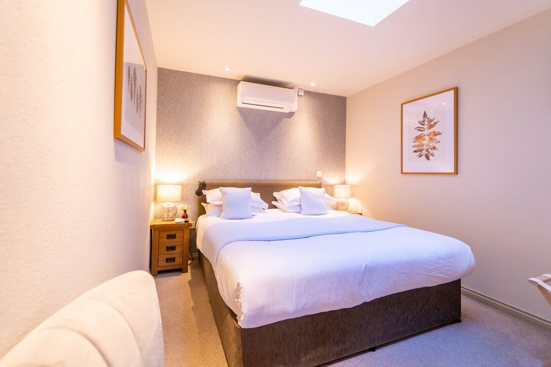 Une chambre à coucher comprenant un lit, des tables de chevet, une commode, un appareil de climatisation et un tableau encadré accroché au mur.