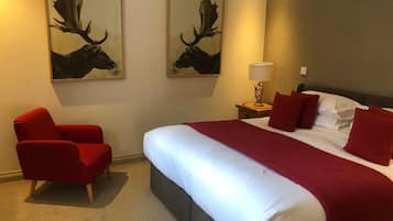 A hotel room with a large bed, red armchair, and two moose paintings on the wall.