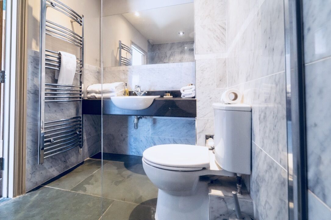 A modern bathroom with a glass shower enclosure, a white toilet, a sink with a black countertop, and marble walls.