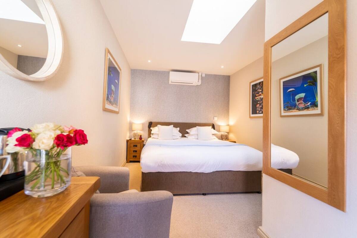 A hotel room with a bed, bedside tables, a mirror, a vase of flowers, and framed pictures on the wall.