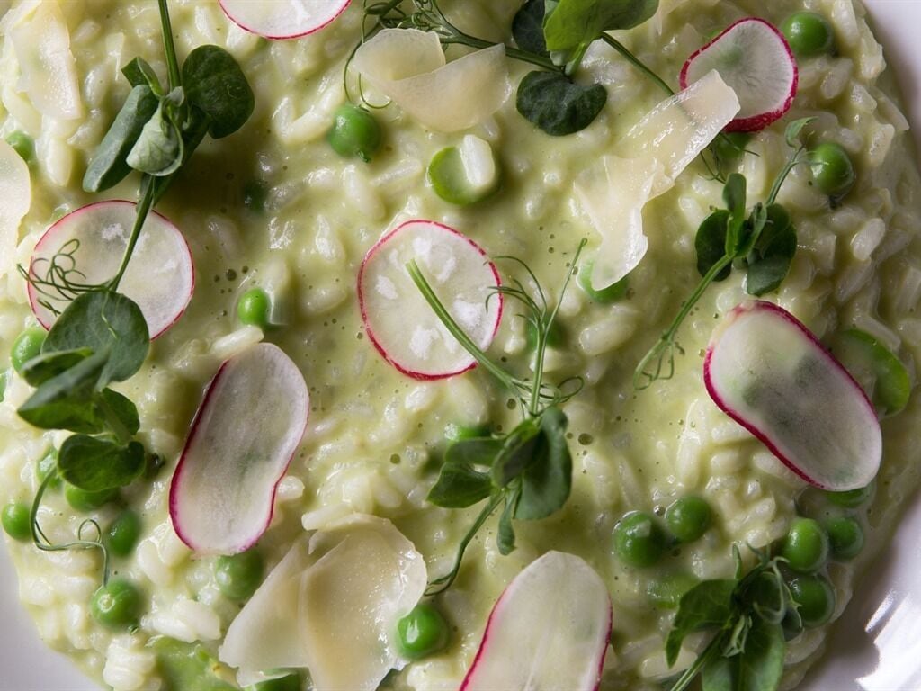 Um close-up de um prato cremoso com ervilhas, rabanetes e ervas.