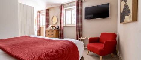 Una habitación de hotel con una cama, un sillón rojo, un televisor, un aparador y una ventana con cortinas.