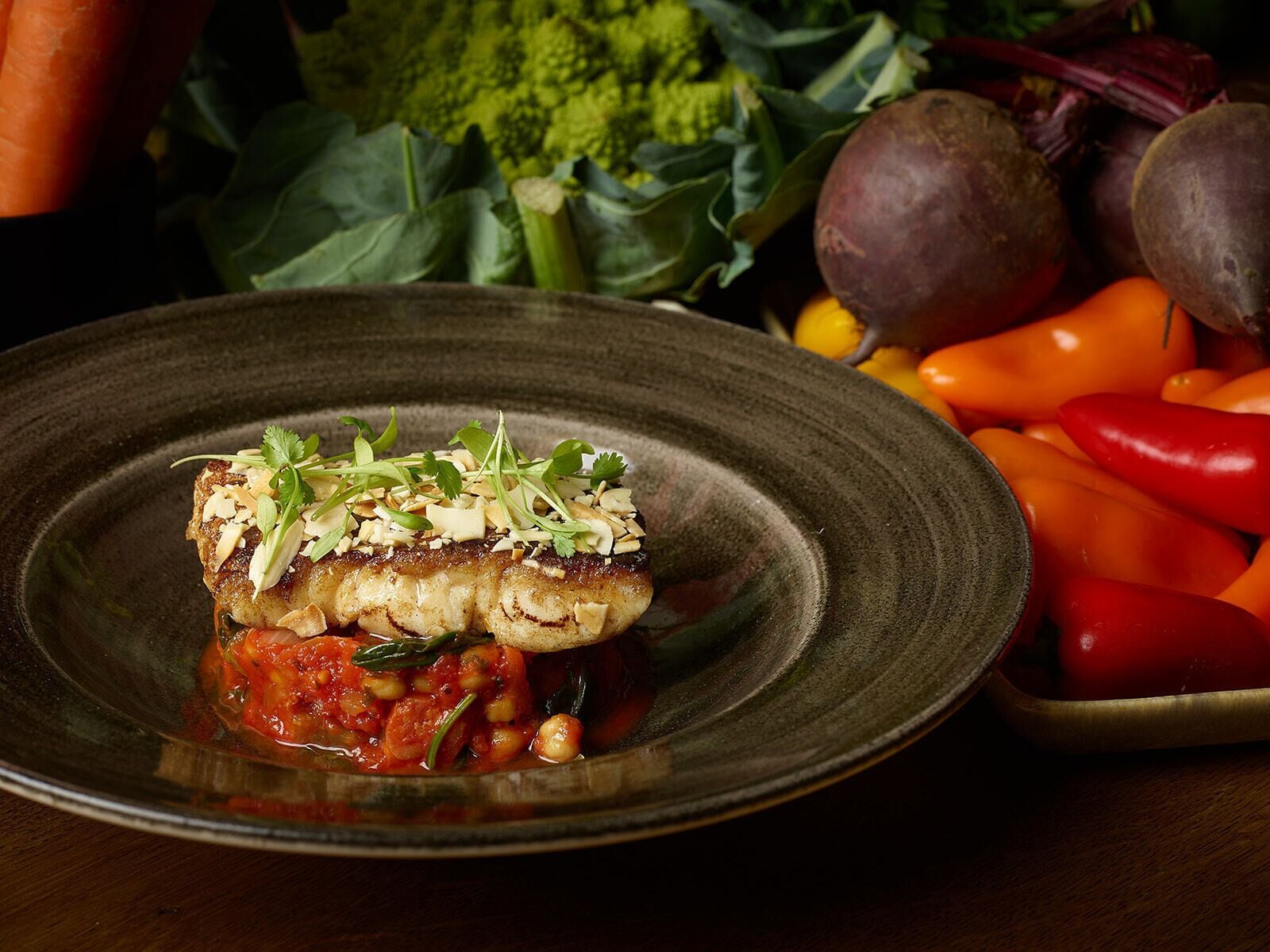 Un plato con un filete de pescado, adornado con hierbas y nueces, acompañado de verduras.
