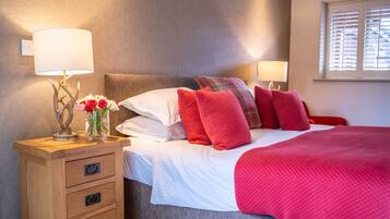 A neatly made bed with red and white bedding, a wooden nightstand with drawers, a vase with flowers, and two wall-mounted lamps.