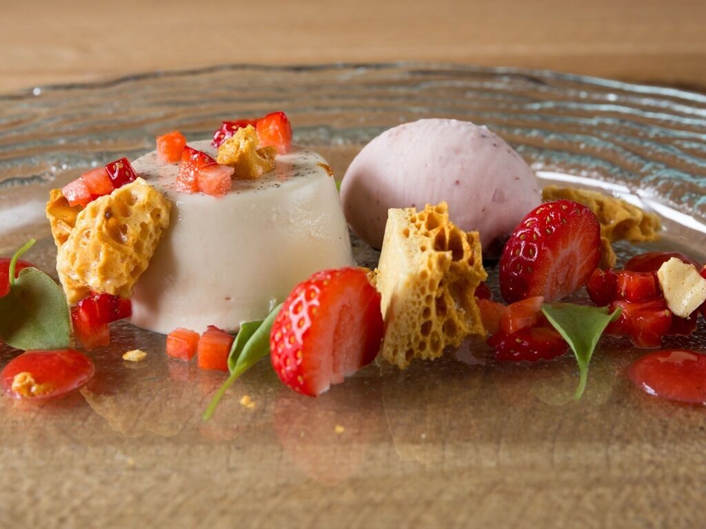 A dessert plate with a panna cotta, a scoop of ice cream, strawberries, and croutons.