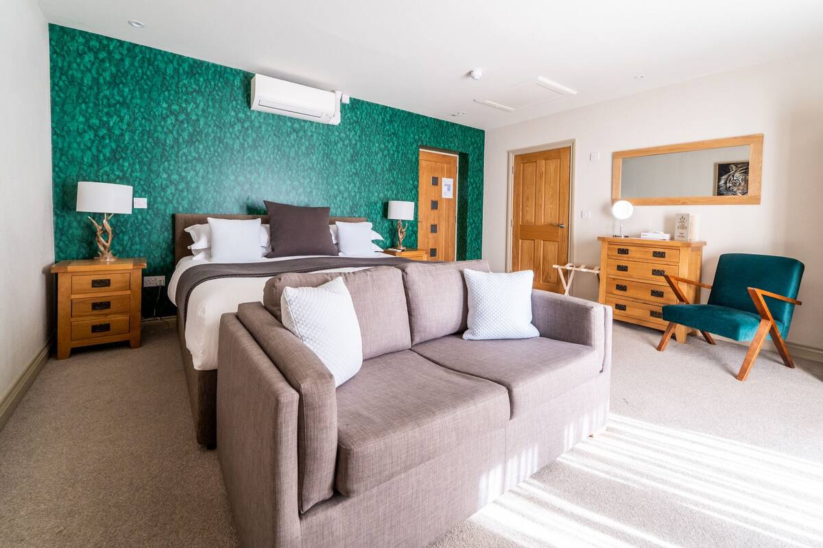 A modern bedroom with a bed, a sofa, a dresser, and a chair.