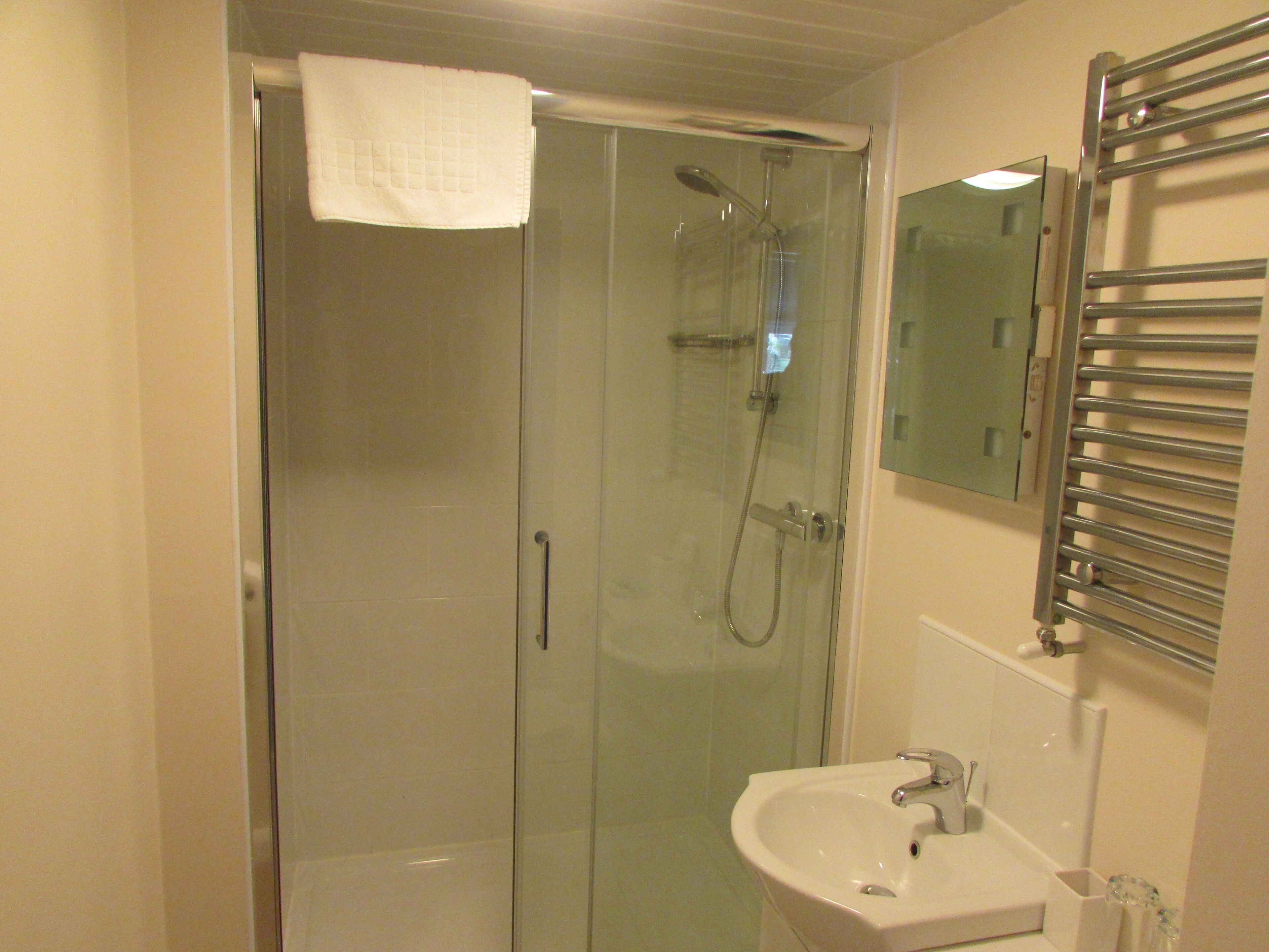 A bathroom with a glass-enclosed shower, a sink, and a towel hanging on the door.