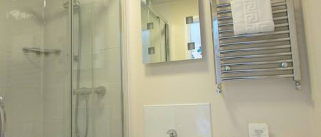 A bathroom with a glass shower enclosure, a sink with a mirror above it, and a towel rack with a towel.