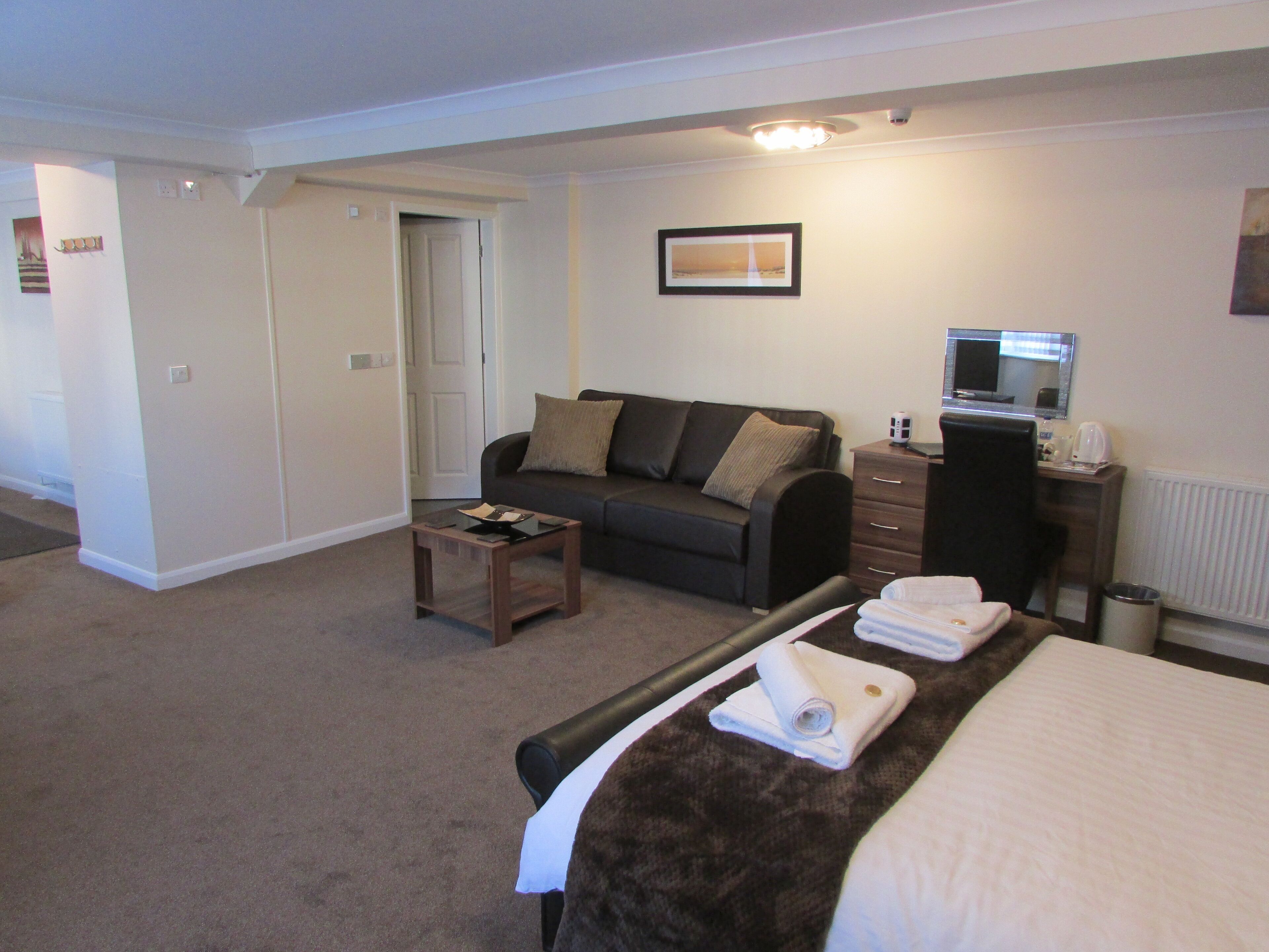 A hotel room with a bed, a sofa, a small table, a dresser, and a television.