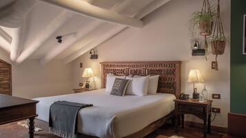 Un dormitorio con una cama grande, cabecera de madera, dos mesitas de noche con lámparas, una planta colgante y un suelo de madera rústica.