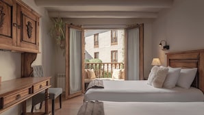 Ein Hotelzimmer mit zwei Betten, einem Schreibtisch, einem Stuhl, einem Fenster mit Blick auf ein Gebäude und einem Balkon.