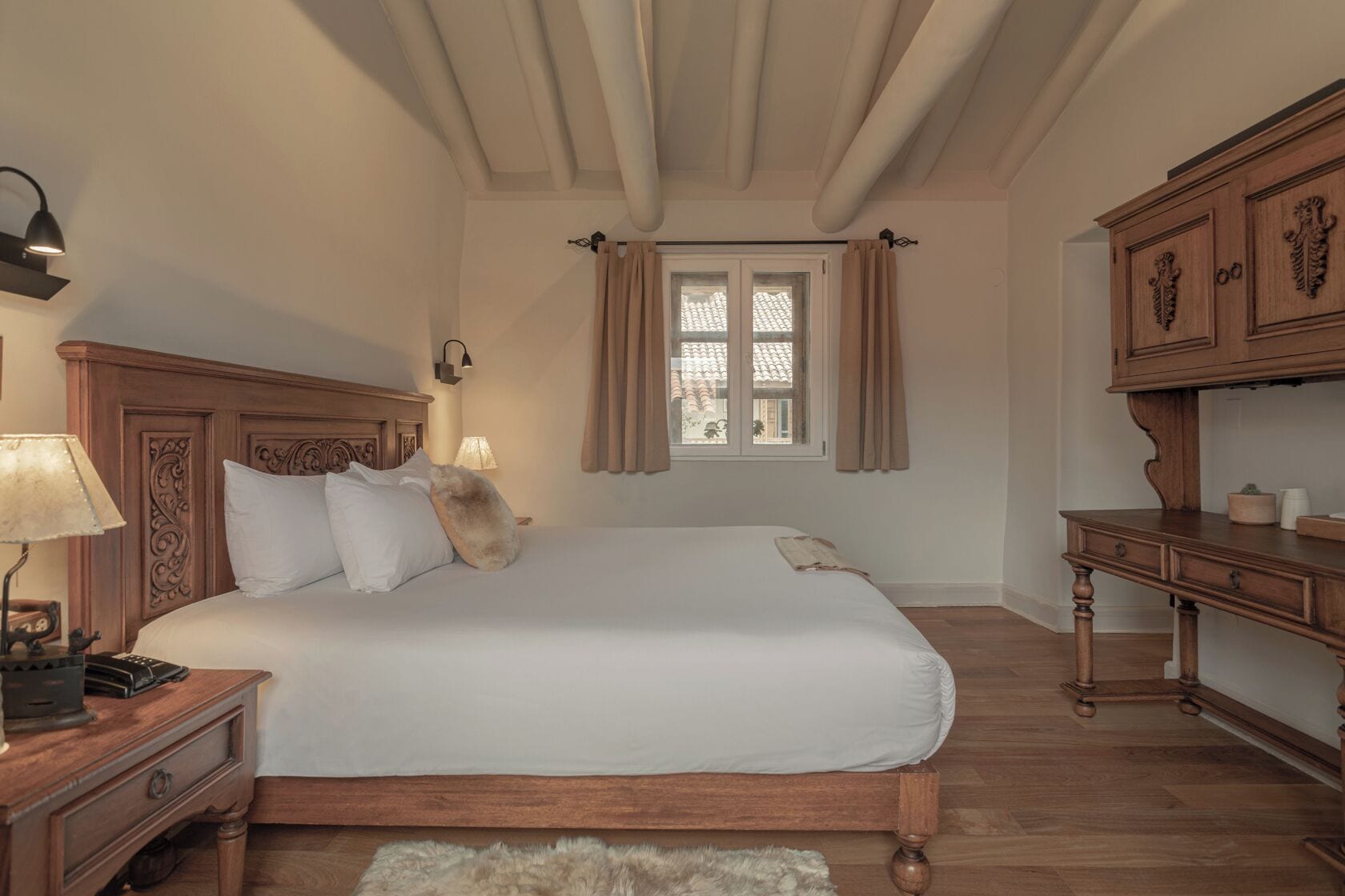 A bedroom with a wooden bed, a nightstand, a lamp, a window with curtains, and a wooden dresser.