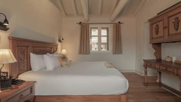 A bedroom with a wooden bed, a nightstand, a lamp, a window with curtains, and a wooden dresser.