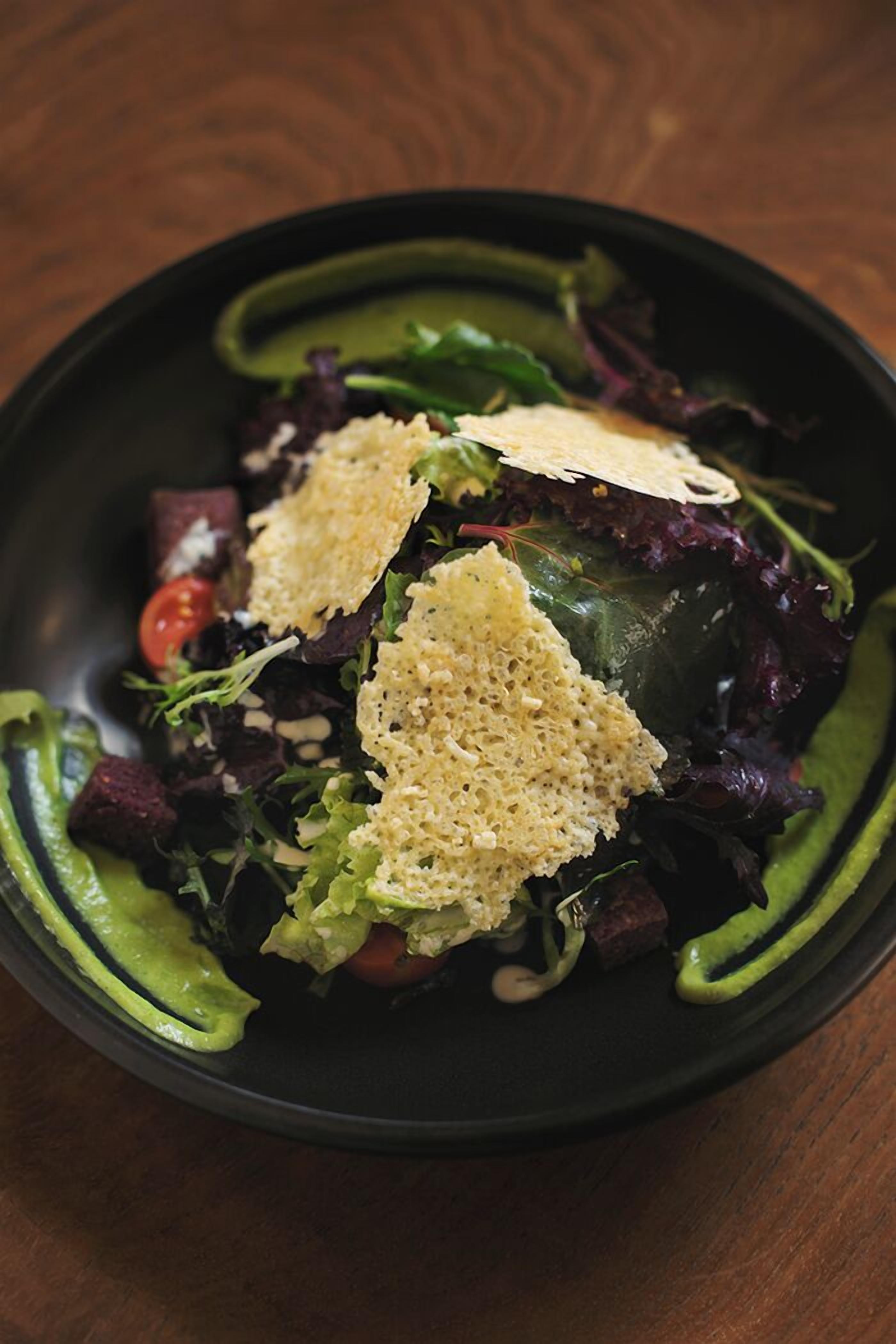 A salad with croutons and a green sauce on a black plate.