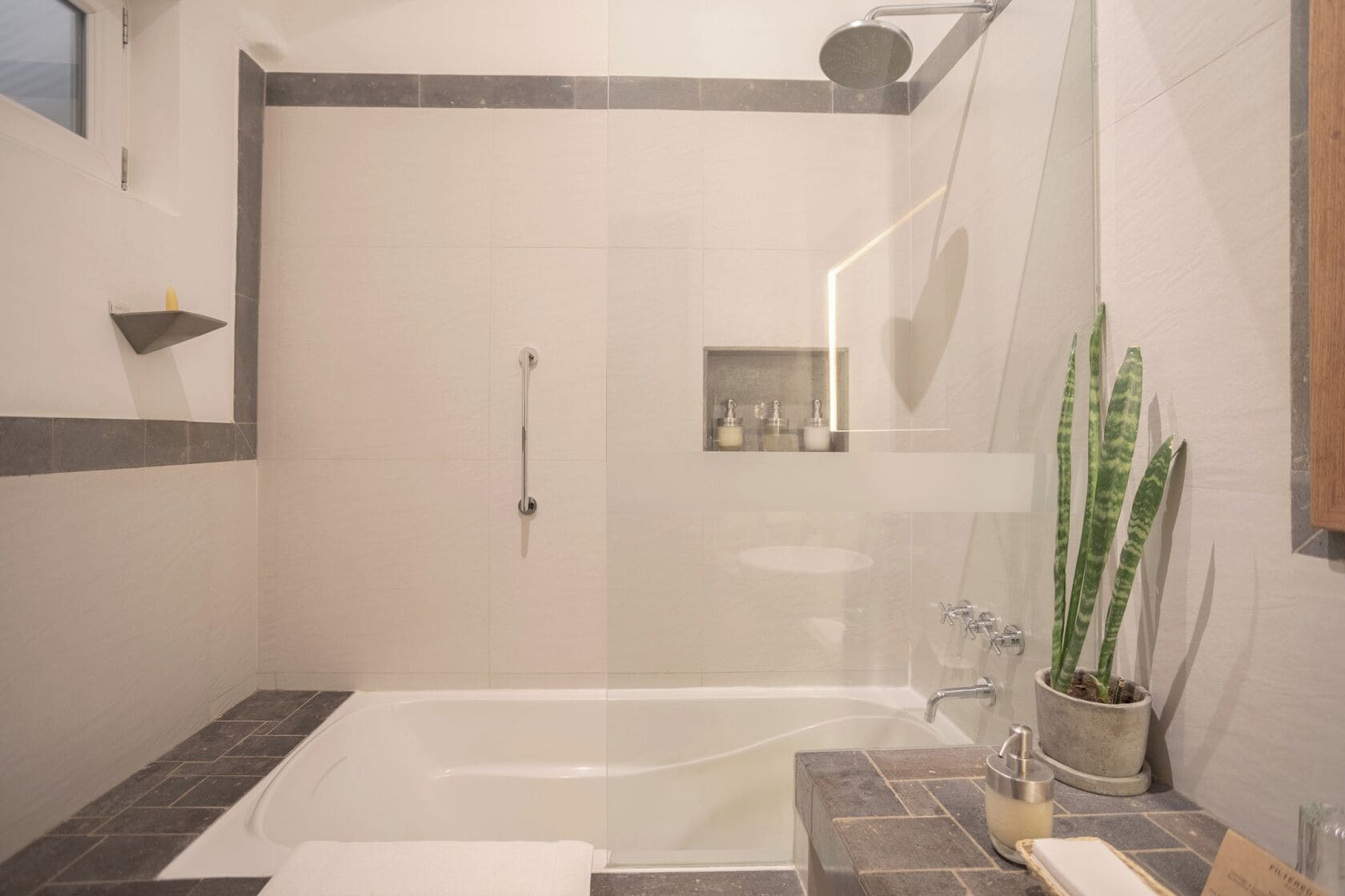 Un baño moderno con ducha a nivel, bañera y una pequeña zona de lavamanos.