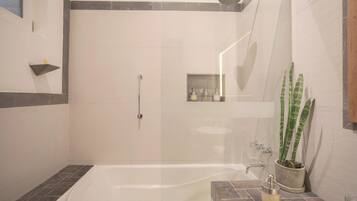 Un baño moderno con ducha a nivel, bañera y una pequeña zona de lavamanos.