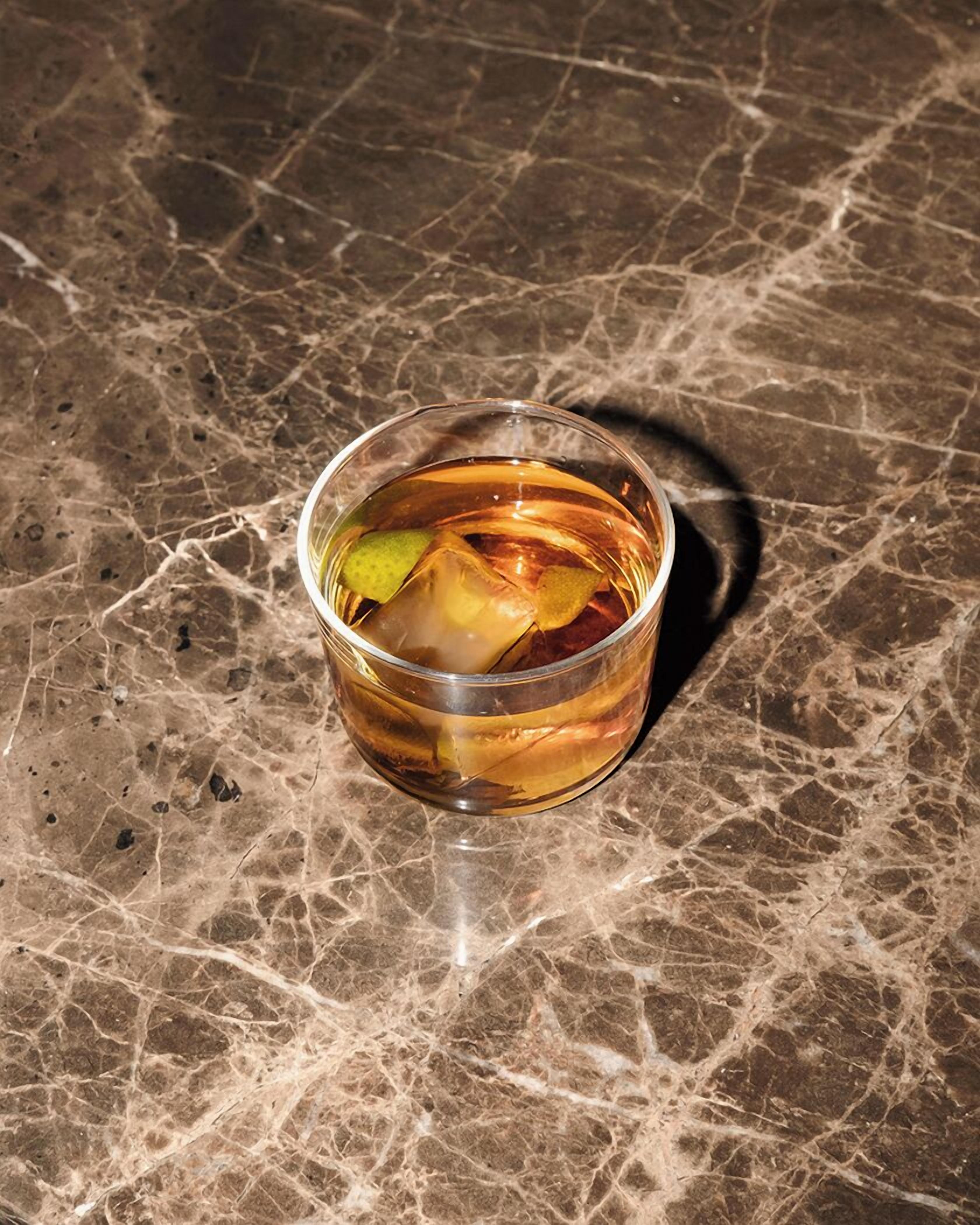 A glass of amber-colored liquid with ice cubes and a lime wedge on a marble surface.
