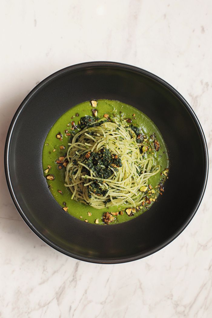 Un plato de pasta con salsa verde y nueces sobre una superficie de mármol.