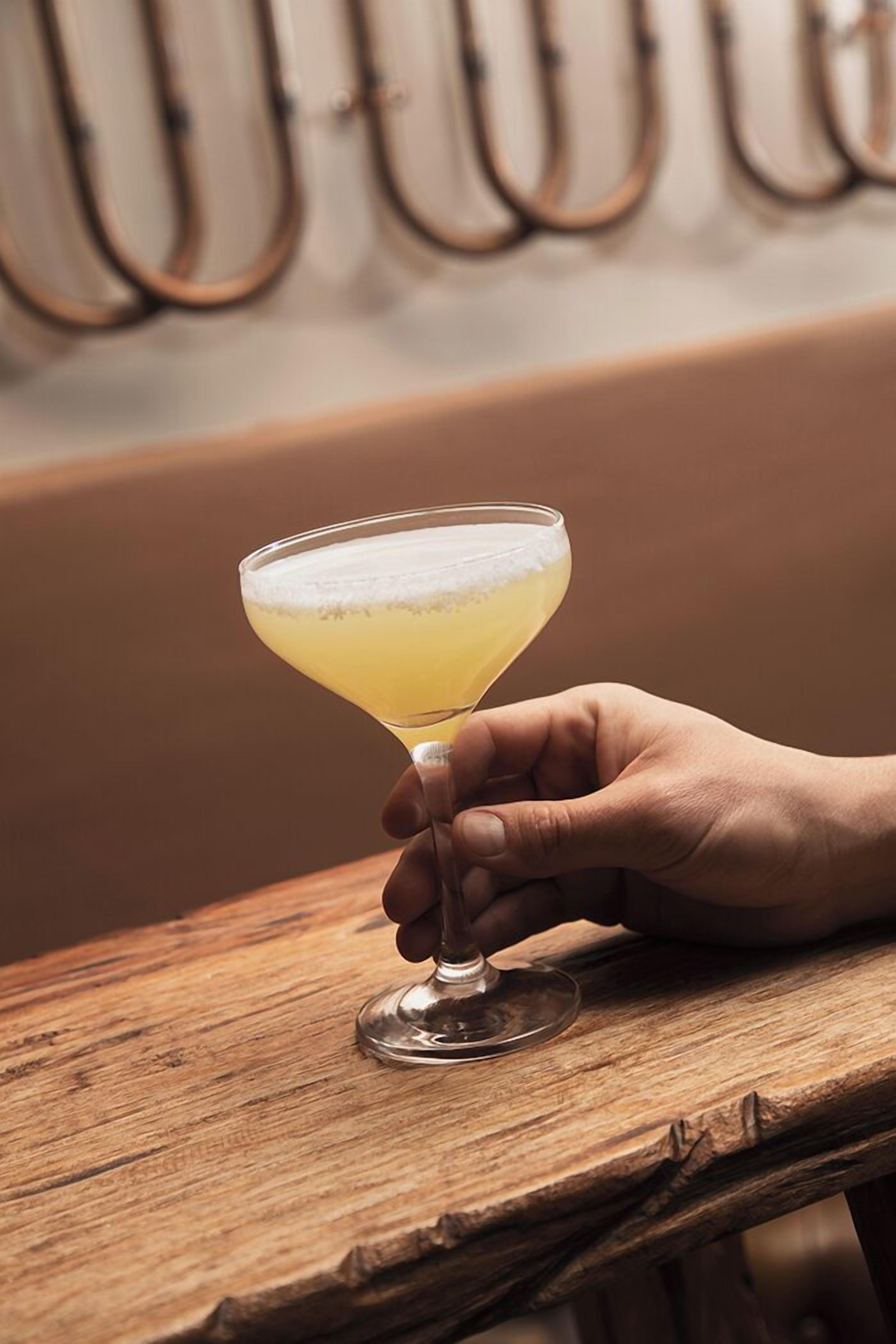A hand holding a cocktail glass on a wooden surface.