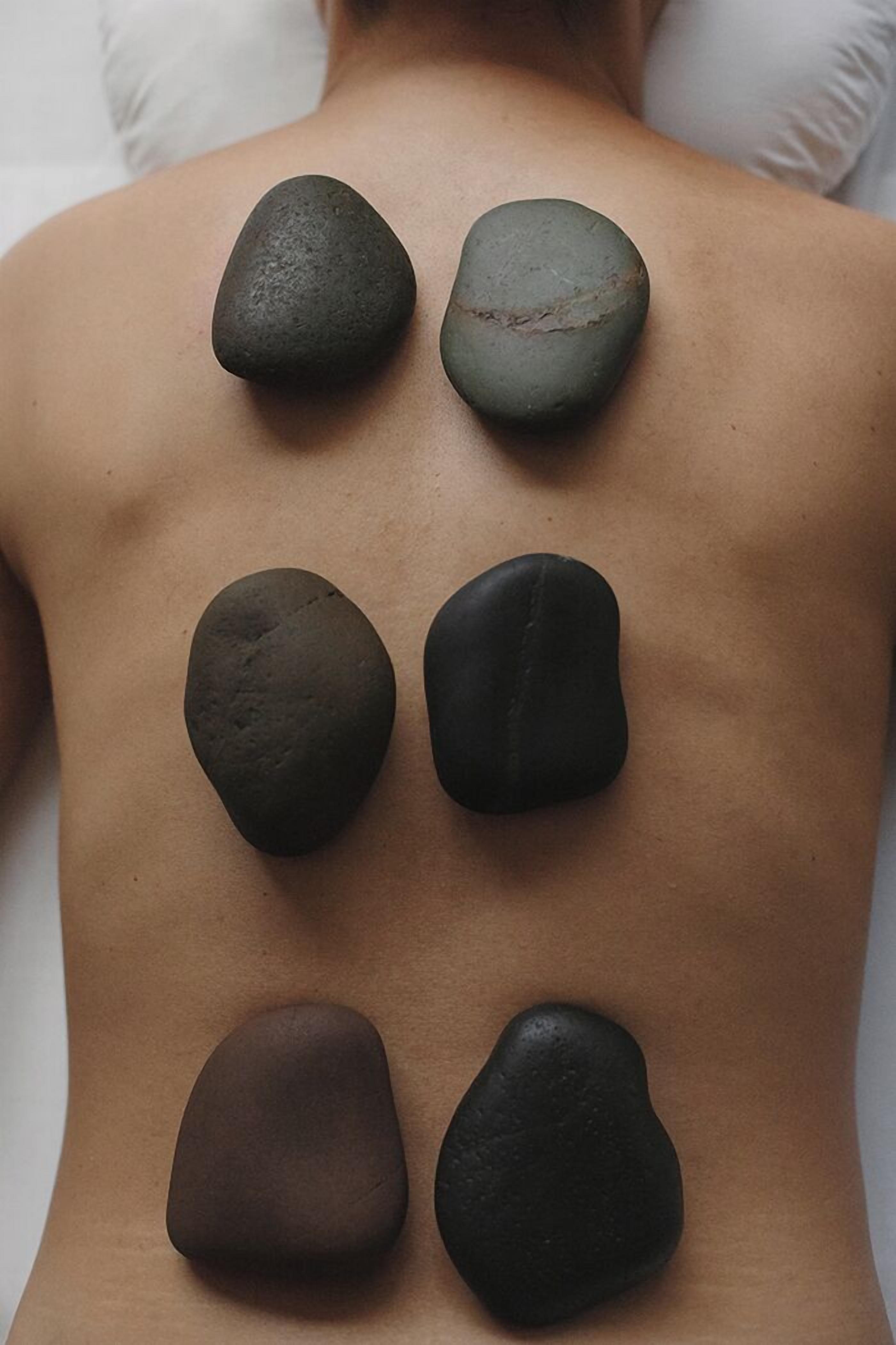 A back view of a person with six smooth stones placed on their back.