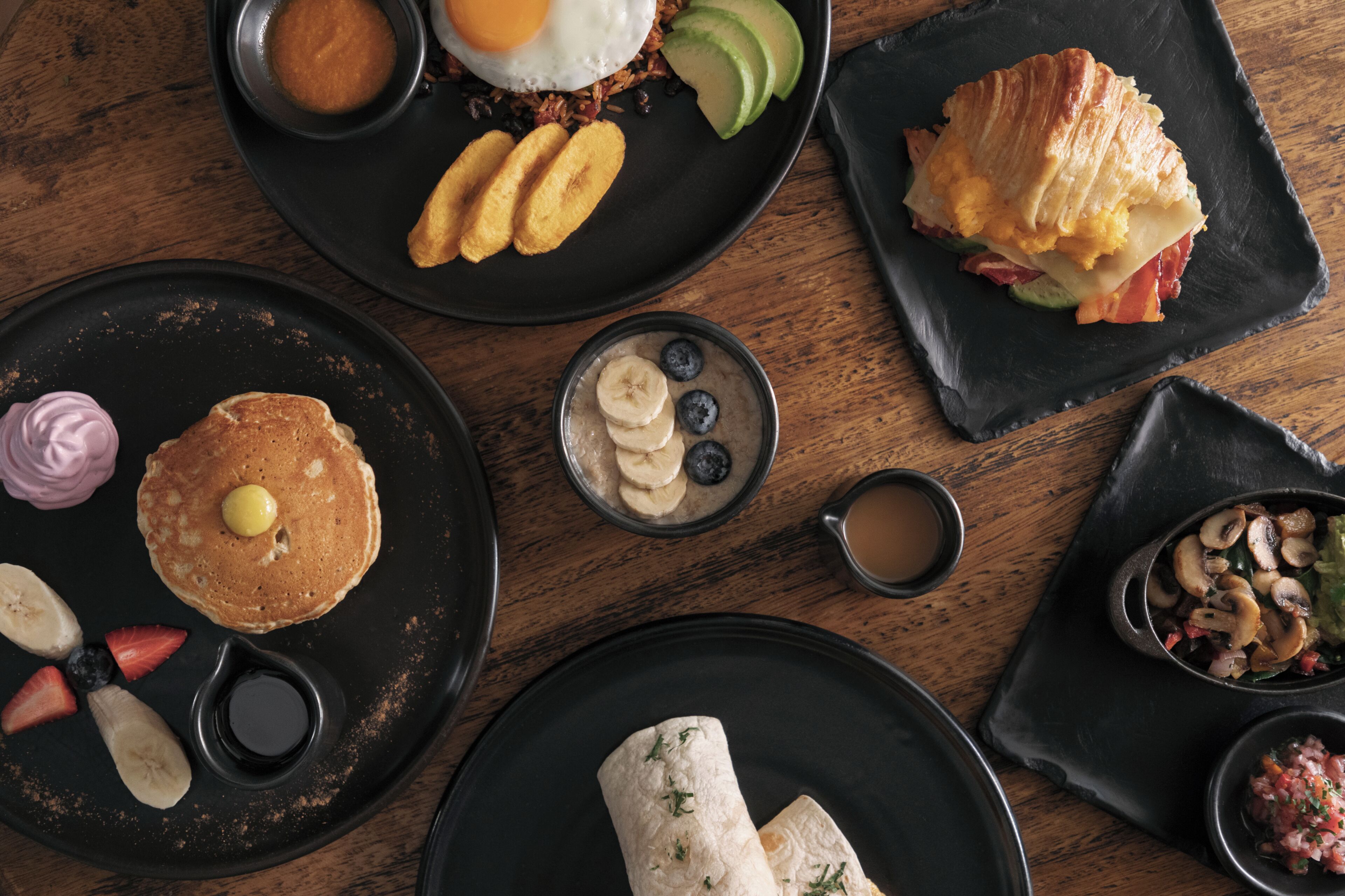 Un copieux petit-déjeuner composé de crêpes, d’œufs et de divers fruits, servi sur une table en bois.