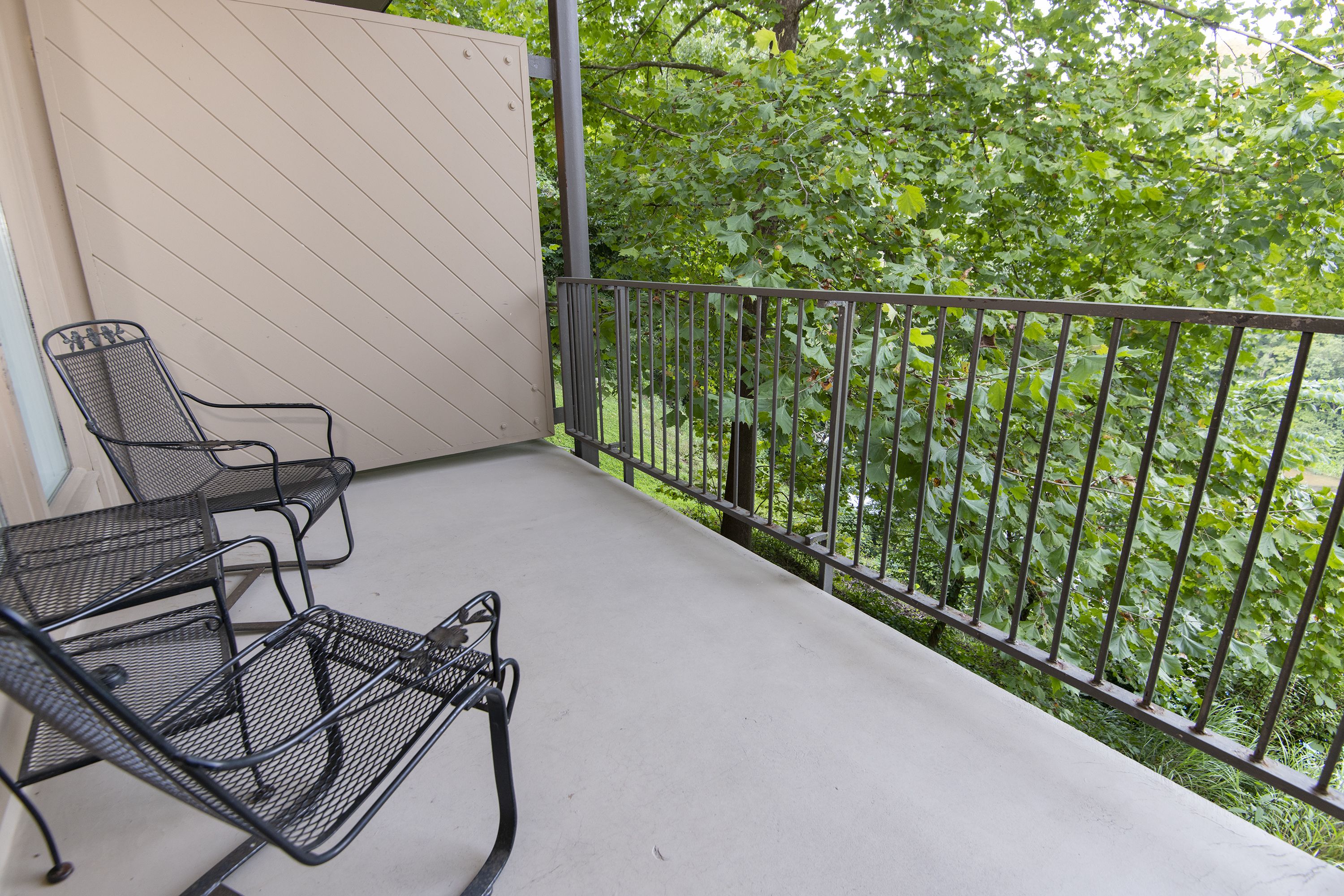 Un balcon avec des chaises en métal et une vue sur un espace verdoyant et arboré.