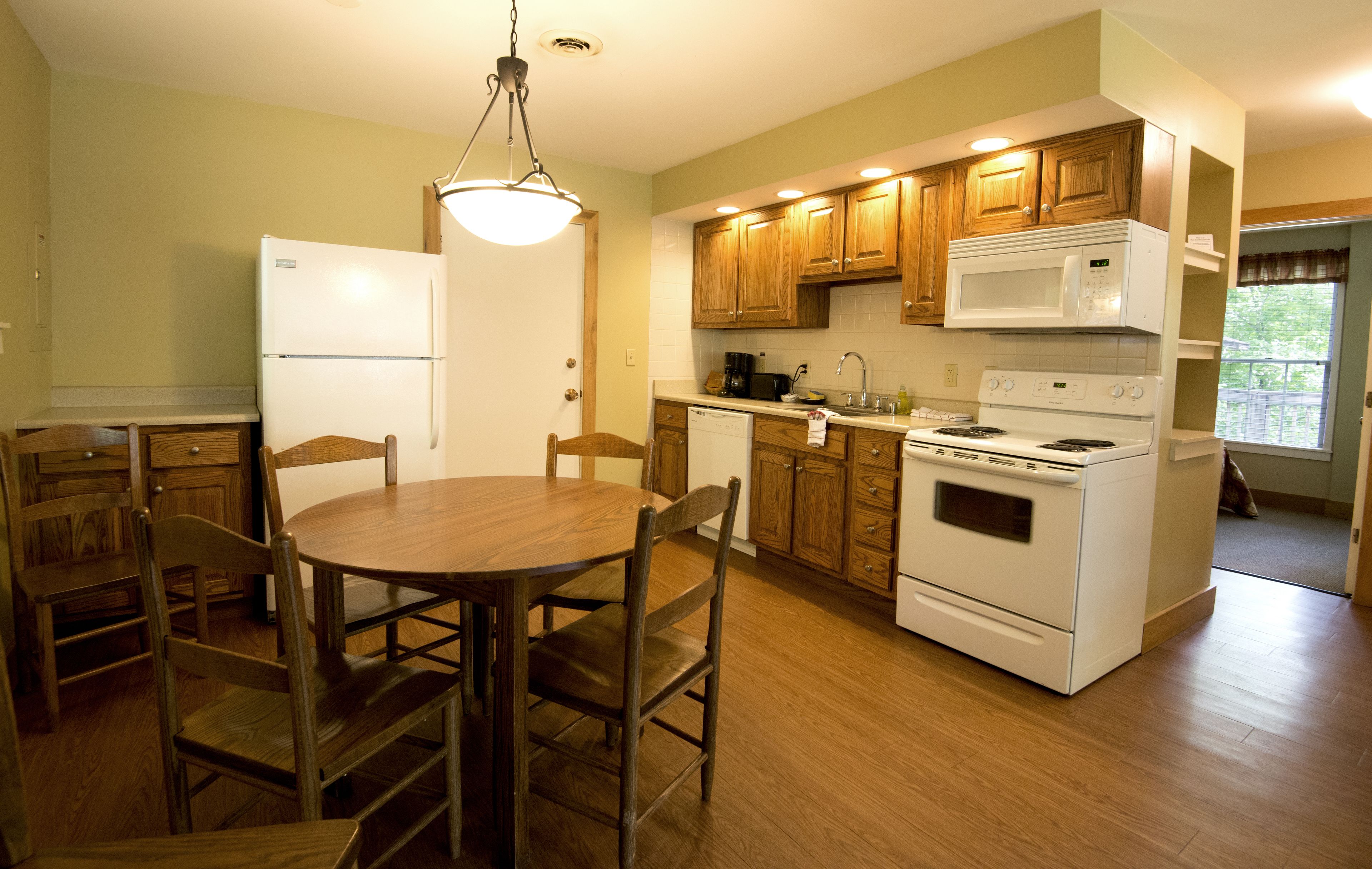 Una cocina con armarios de madera, un refrigerador blanco, una estufa y una mesa de comedor con sillas.