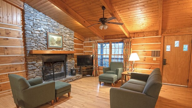 A log cabin interior with a stone fireplace, wooden walls, and a ceiling fan. - Natural Bridge State Resort Park (Slade)