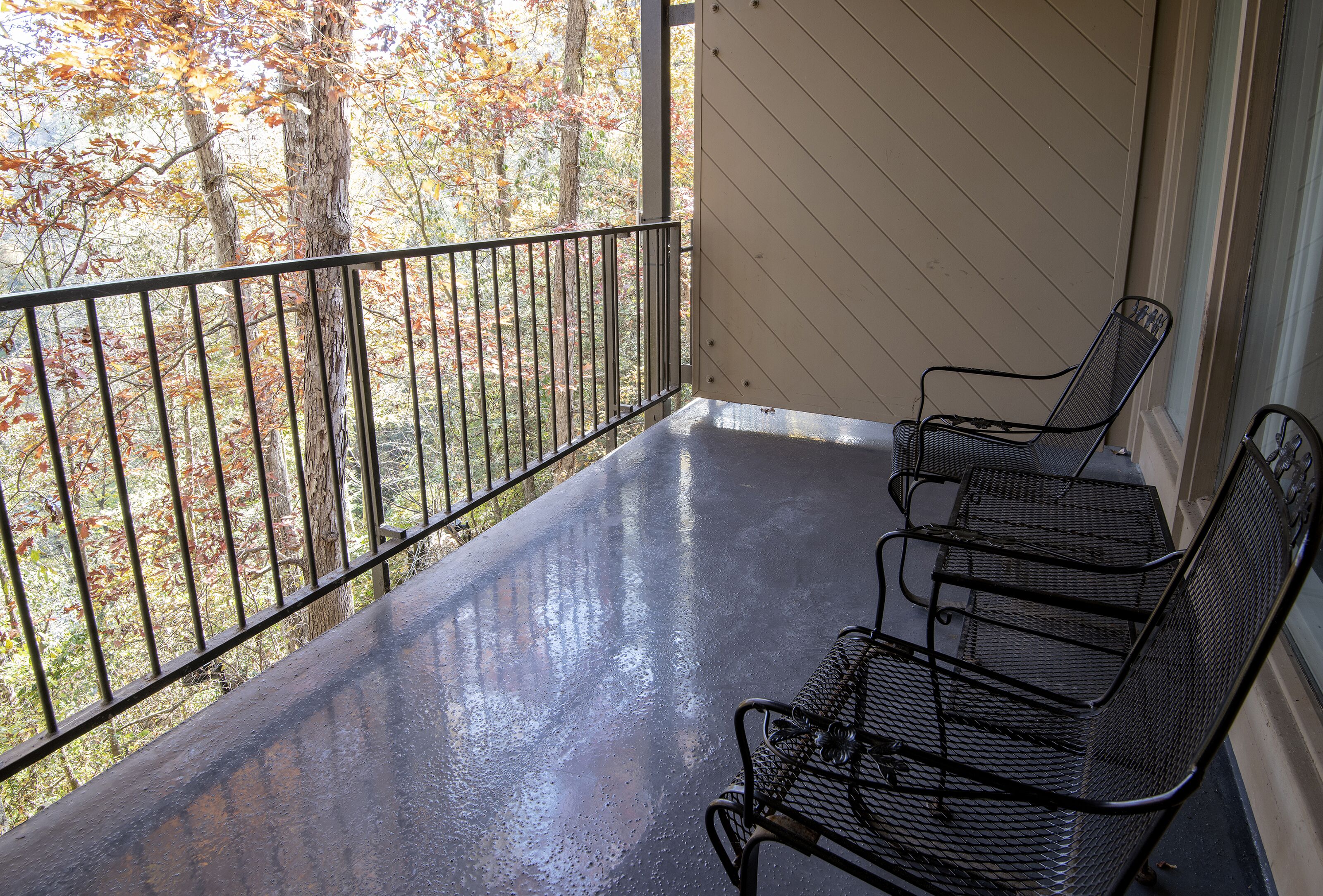 A covered porch with a metal railing and two metal chairs.