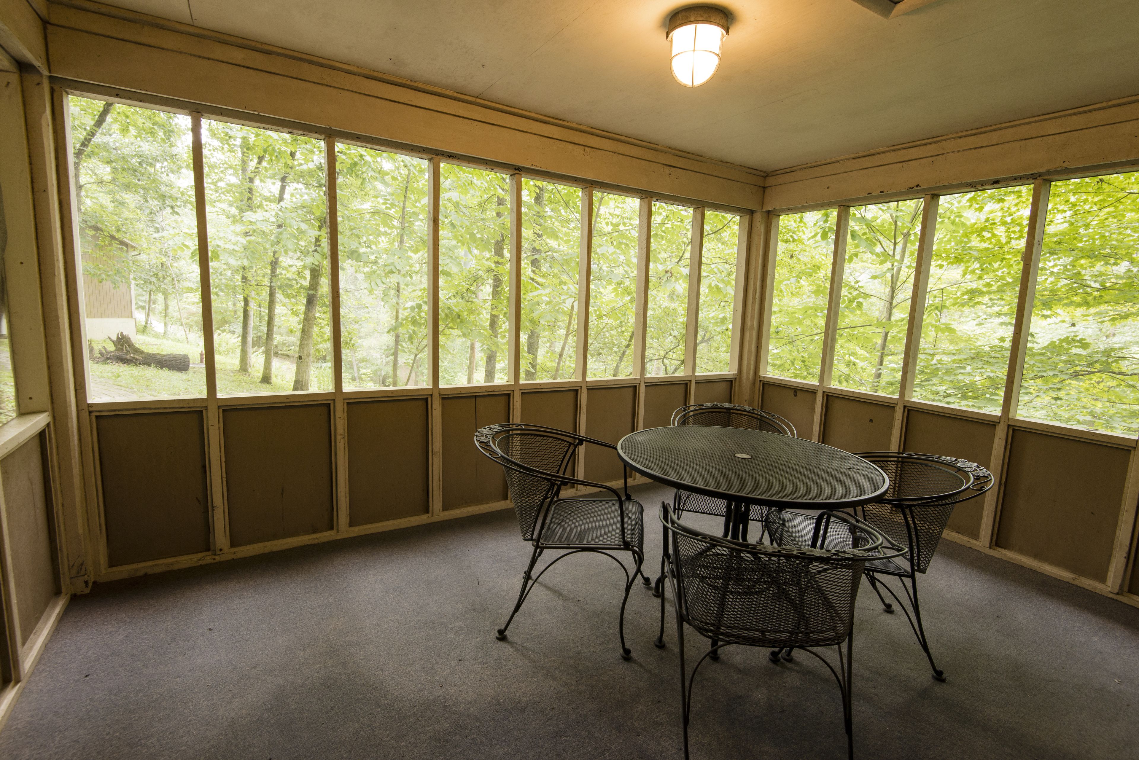 A covered patio with a table and four chairs, large windows, and a ceiling light.