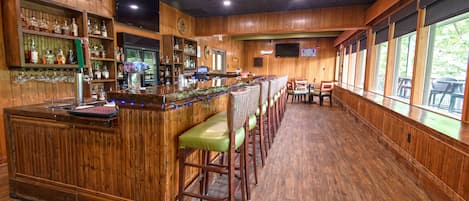 Uma área de bar com paredes de madeira, um balcão comprido e vários bancos.